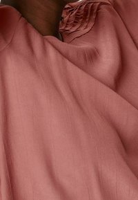 Rosa-pink Stoff mit einer weichen, strukturierten Oberfläche und subtilen vertikalen Linien, ausgestattet mit einem gerafften Ausschnitt. Der Fall ist fließend und glatt.