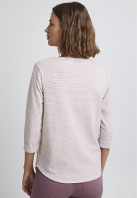 Lichtroze, langemouwen shirt met een textuurpatroon en een ronde zoom. De achterkant heeft een subtiel ruitpatroon en een bootnek.