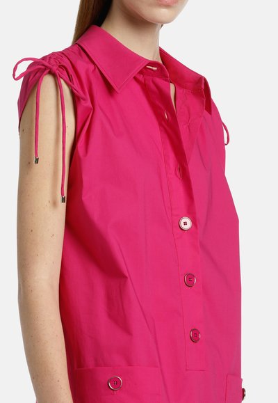 Camicia di cotone fucsia con colletto, maniche corte, dettagli con coulisse sulle spalle e chiusura con bottoni frontale. Due tasche frontali.