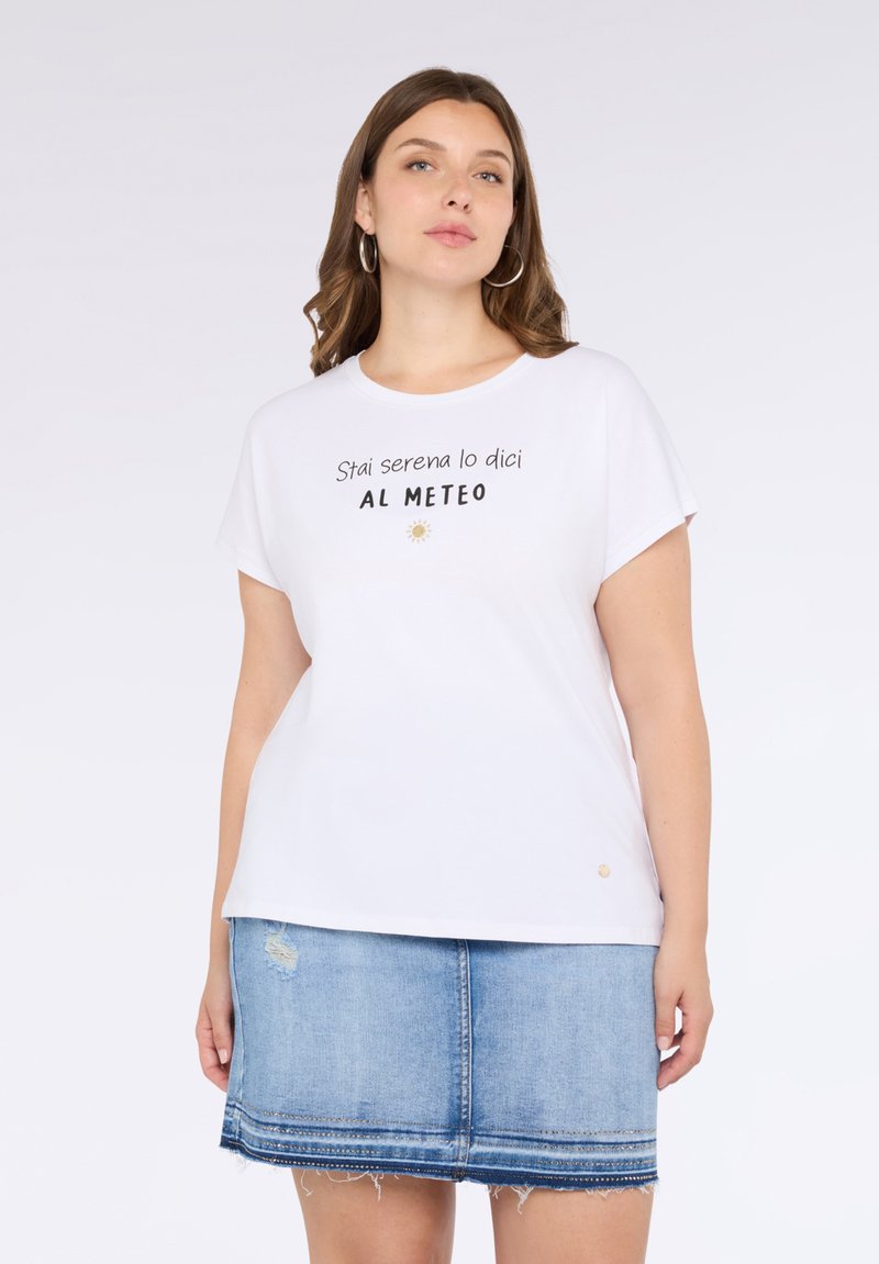 Camiseta blanca de manga corta con texto negro que dice "Stai serena lo dici AL METEO" y un gráfico de sol. Combinada con una falda de mezclilla.