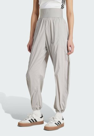 Pantalones de color gris claro, sueltos, con una cinturilla elástica alta, tobillos recogidos y una textura suave y brillante. Combinados con zapatos y calcetines blancos.