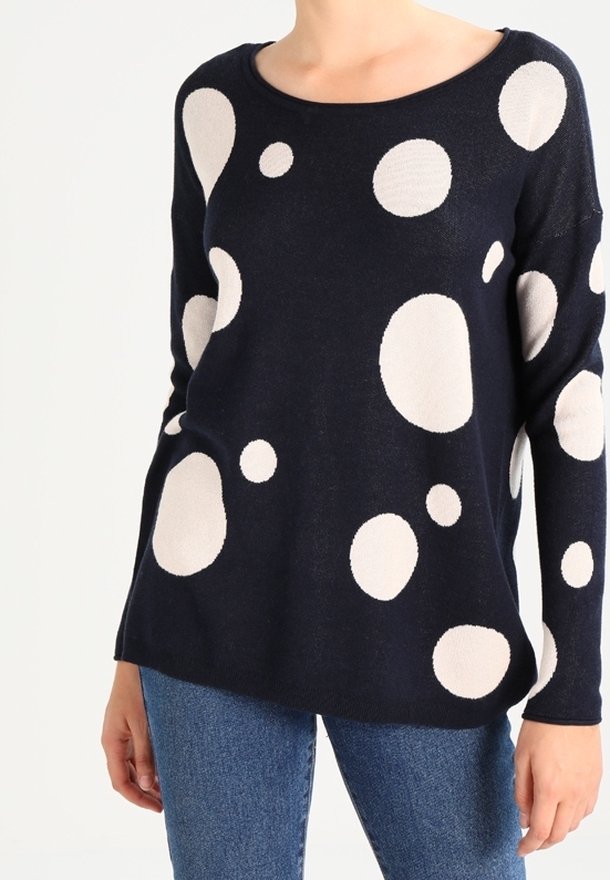 Navy sweater featuring large cream polka dots, round neckline, soft texture, and relaxed fit. Paired with denim jeans.