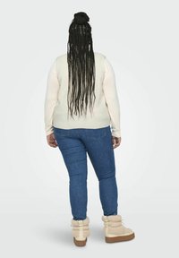 Ljuskrämfärgad, strukturerad väst över en långärmad skjorta, kombinerad med blå jeans och beige, fluffiga knähöga stövlar med tjock sula.