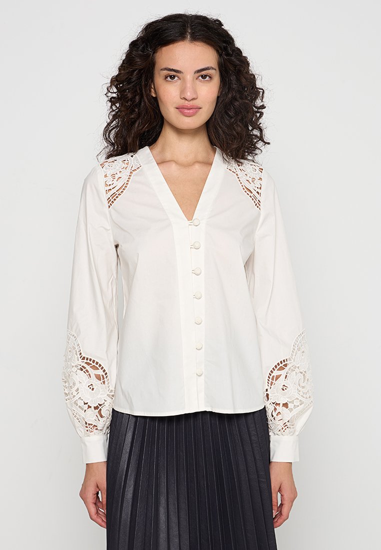 Weiße Bluse mit langen Ärmeln, mit dekorativen Spitzenakzenten an den Schultern und Manschetten sowie einer Knopfleiste vorne.