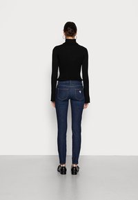 Jersey de cuello alto de rayas negras combinado con jeans ajustados de color azul oscuro. Los detalles notables incluyen bolsillos traseros y un pequeño logo de la marca. Zapatos negros completan el conjunto.