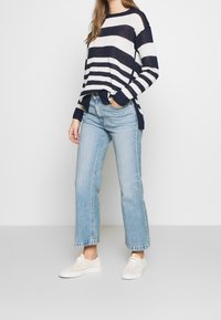 Navy and white striped knit sweater with side slits, paired with light blue high-waisted jeans and beige sneakers.