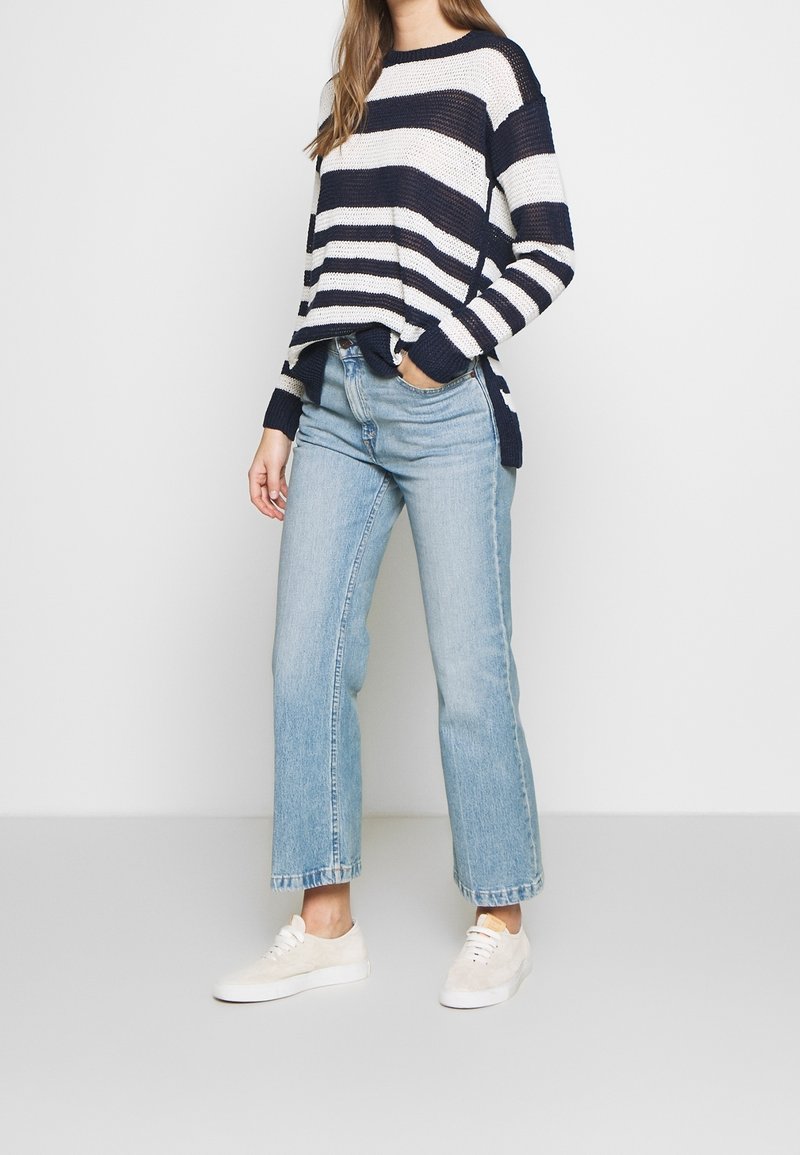 Navy and white striped knit sweater with side slits, paired with light blue high-waisted jeans and beige sneakers.