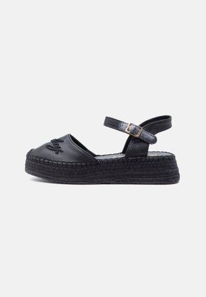 Schwarze Sandale mit strukturierter Plateausohle, Knöchelriemen und goldener Schnalle, geschlossener Zehenbereich mit gesteppter Frontdetail und gewebter dicker Sohle.