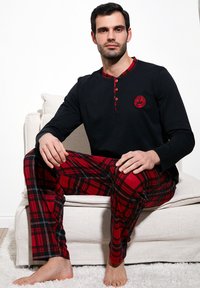 Sort langærmet pyjamasoverdel med røde ternede accenter og knapper. Røde ternede pyjamastights med sorte og hvide linjer. Blød tekstur.