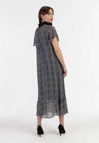 Abito maxi a fantasia bianco e nero con maniche a campana corte, orlo arricciato e colletto nero. Il modello indossa tacchi neri.