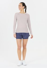 Langärmliges, hellrosa Oberteil mit schmaler Passform und gerippter Textur, kombiniert mit navyblauen Shorts. Weiße Sportschuhe runden das Outfit ab.
