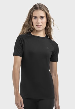 Junge Frau mit langen Haaren, die ein schlichtes schwarzes Sportshirt mit kurzen Ärmeln vor weißem Hintergrund trägt.