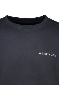 Sudadera de algodón negra con cuello redondo. Presenta un logotipo bordado en blanco "JUNK de LUXE" en el lado izquierdo. Textura suave.