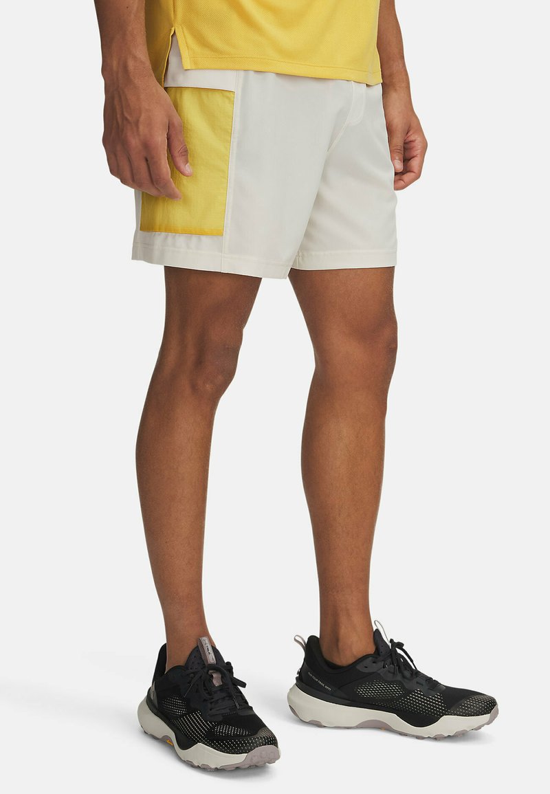 Herren Shorts aus hellgrauem Material mit einer gelben Seitentasche. Bequeme Passform und knielange Länge. Kombiniert mit schwarzen Sneakers.