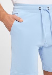Light blue cotton shorts with an elastic waistband, drawstring, and side pocket. Smooth texture with reinforced stitching details.