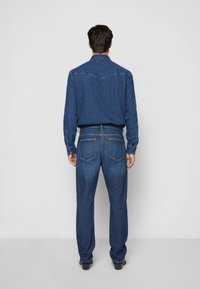 Denim shirt and pants set in dark blue. Shirt features a classic collar and buttoned cuffs; pants have rear pockets and a straight leg design.