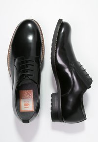 Chaussures habillées en cuir noir avec finition polie, à lacets, à bout rond, et semelle marron contrastée. Présentent des détails de couture minimaux.