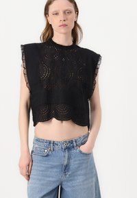 Top nero croppato con orlo scallop, dettagli con motivi ad occhio e maniche arricciate, abbinato a jeans azzurri a vita alta.