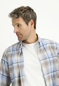 Knopen-over flanellen overhemd in lichtblauw, bruin en wit geruit patroon, met een losse pasvorm en een button-down kraag over een grijs T-shirt.