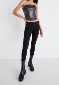 Top in pelle nera a bustier con design strutturato, abbinato a jeans skinny neri a vita alta. Stivali neri con tacco chunky completano il look.