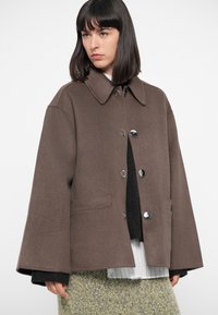 Brown wool-blend jacket with a collared neck, front buttons, and side pockets. Features wide sleeves and a loose silhouette.