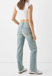 Ljust blålila denimjeans med rak passform och bakfickor, bärs med en kortärmad vit topp och silverfärgade sportskor.