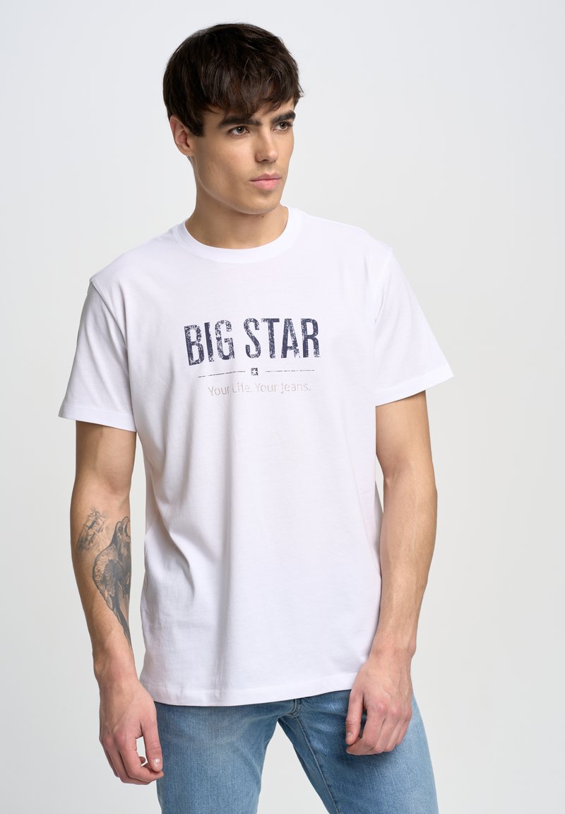 Camiseta blanca de algodón con cuello redondo, que presenta una impresión frontal en azul marino con la leyenda "BIG STAR" y "Tu Vida. Tus Jeans." en una fuente clásica.