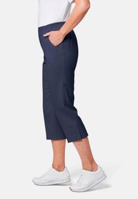 Marineblauwe capri-broek met elastische tailleband en zijzakken, voorzien van een soepele textuur en een zoom met drie decoratieve knopen.