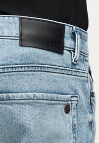 Τζιν παντελόνι σε ανοιχτό μπλε χρώμα με μαύρο δερμάτινο λογότυπο "BOSS" στη μέση και μικρό μεταλλικό λογότυπο του brand στην πίσω τσέπη.