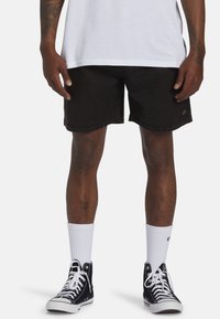 Pantalones cortos de denim negro con un corte recto, con un sutil parche con el logo en el costado. Combinados con calcetines blancos hasta el tobillo y zapatillas altas negras.