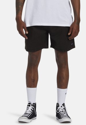 Pantalones cortos de denim negro con un corte recto, con un sutil parche con el logo en el costado. Combinados con calcetines blancos hasta el tobillo y zapatillas altas negras.