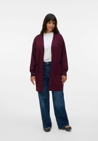 Dug burgundski kardigan s otvorenim prednjim dijelom, dva džepa i opuštenim krojem. Uparen s bijelim T-shirtom i širokim trapericama.