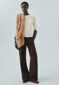 Pull crème avec une douce écharpe en fausse fourrure marron, associé à un pantalon marron à jambes larges et des gants en cuir noir. Textures lisses et tons chauds.