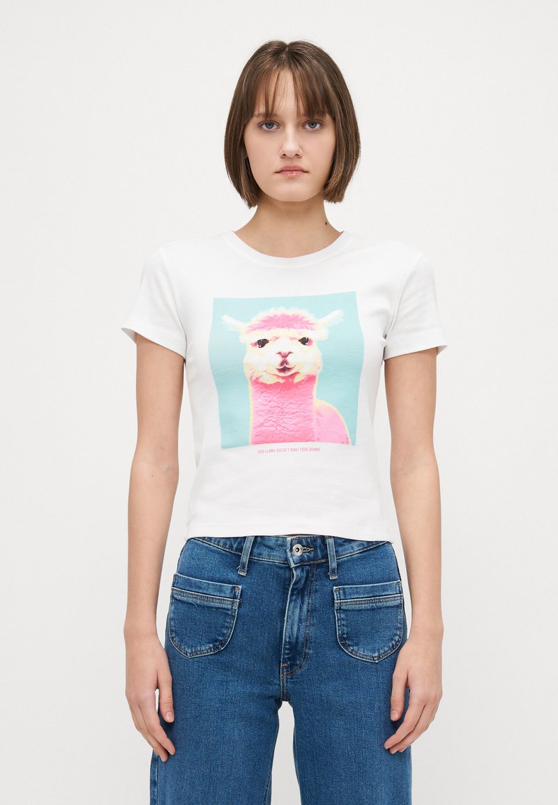 T-shirt en coton blanc avec un motif carré représentant un design coloré d'alpaca et du texte. Coupe décontractée avec des manches courtes et un col rond.