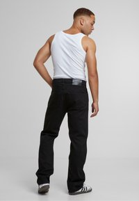 Schwarze Denim-Jeans im geraden Schnitt, mit Gesäßtaschen und einem Lederlabel am Bund. Das Modell trägt ein weißes Tanktop.
