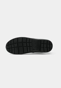 Semelle de chaussure en caoutchouc noir avec un motif de semelle profond, comportant des rainures carrées et rectangulaires pour l'adhérence et la flexibilité. Design à bords plats.