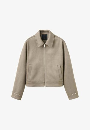 Jachetă bej scurtă, realizată dintr-un material neted, cu guler ascuțit, închidere cu fermoar și accente cu ținte pe guler și mâneci.