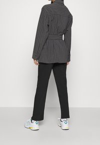 Blazer a rayas grises con cintura ceñida, combinado con pantalones negros y zapatillas blancas con acentos en azul y amarillo.