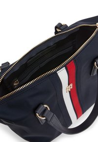 Borsa in nylon blu con hardware dorato, caratterizzata da strisce verticali rosse e bianche. L'interno include tasche e una fodera testurizzata. Chiusura con zip.