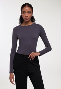 Maglietta a maniche lunghe, attillata, in tessuto grigio scuro con scollatura rotonda, abbinata a pantaloni jogger neri con vita elasticizzata.