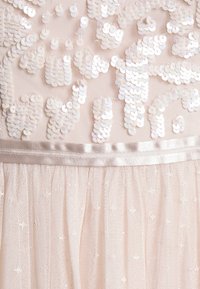 Tissu rose pâle avec des sequins blancs irisés disposés en motifs abstraits et une bordure en ruban de satin brillant au-dessus de couches de tulle transparent.