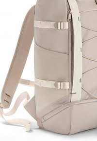 Világos bézs hátizsák texturált anyagból, állítható pántokkal, oldalsó zsebbel és megerősített varrással; minimalista dizájnnal rendelkezik, funkcionális hardverelemekkel.
