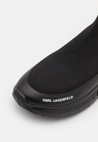 Baskets noires avec une tige en tricot texturé, un bout rond et une semelle en caoutchouc lisse avec le logo "Karl Lagerfeld" en blanc.