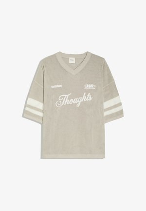 Beige neulottu lyhythihainen neule V-pääntiellä, valkoiset raidat hihoissa ja teksti "Thoughts" isolla käsinkirjoituksella edessä.