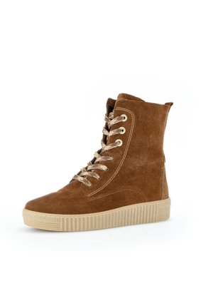 Brązowy zamszowy sneaker za kostkę z beżowymi sznurowadłami i grubą beżową gumową podeszwą, ustawiony pod kątem w lewo na białym tle.