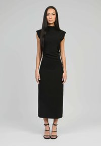 Robe noire ajustée avec des manches courtes en forme de cap, un col haut et une longueur au genou. Texture lisse et design minimaliste, complétée par des talons à lanières.
