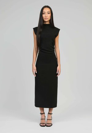 Robe noire ajustée avec des manches courtes en forme de cap, un col haut et une longueur au genou. Texture lisse et design minimaliste, complétée par des talons à lanières.