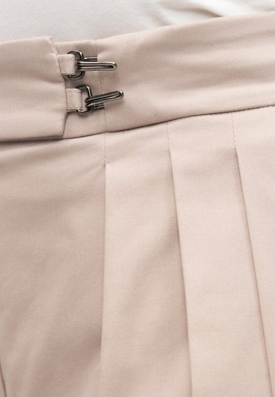 Φούστα σε απαλό ροζ χρώμα με πιέτες, με δύο ασημένιους γάντζους στο ύψος της μέσης, κατασκευασμένη από ένα απαλό ύφασμα με διακριτή υφή.