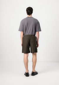 T-shirt gris à manches courtes associé à un short olive vert avec taille élastique. Des chaussures noires complètent la tenue. Design simple avec des éléments pratiques.