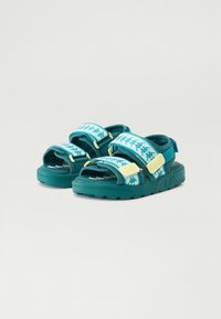 Sandali aperti turchesi e bianchi con cinturini regolabili, caratterizzati da un motivo logo ripetuto e suole imbottite.